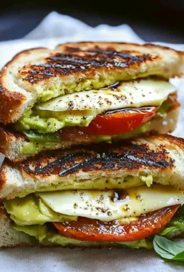 Avocado, mozzarella, and tomato grilled cheese sandwich on a wooden board.