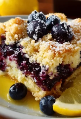 A slice of Lemon Blueberry Cheesecake Dump Cake topped with fresh blueberries and lemon zest.
