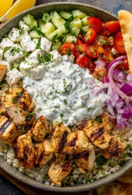 Delicious Greek chicken rice bowl topped with fresh cucumbers and tzatziki sauce.