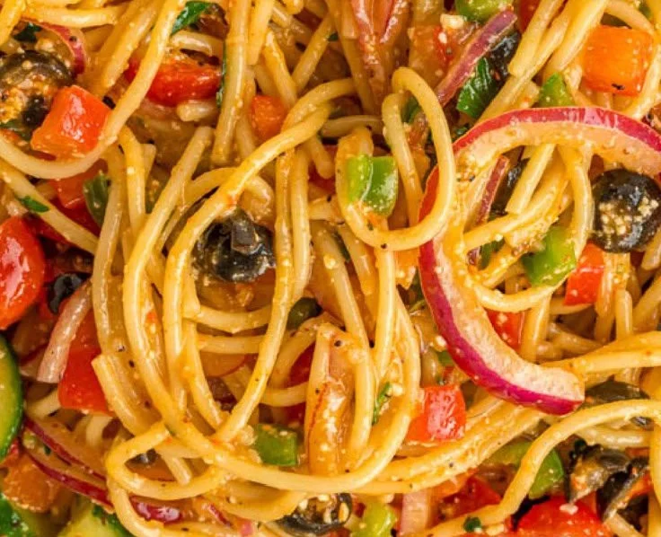 A vibrant bowl of spaghetti salad with vegetables and dressing