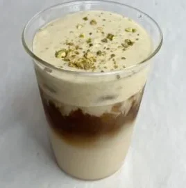 Cup of delicious pistachio cream latte topped with whipped cream and nuts
