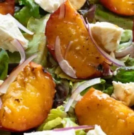A colorful grilled peach salad with greens and dressing
