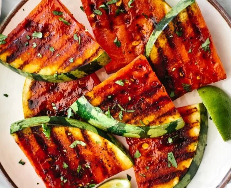 Grilled watermelon slices drizzled with honey and lime juice on a plate.
