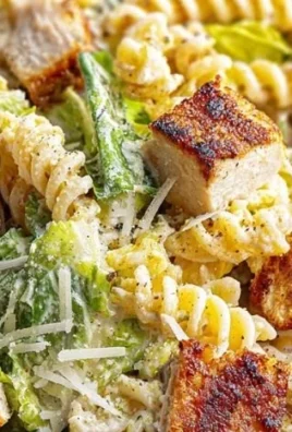 Chicken Caesar Pasta Salad in a bowl with fresh herbs and toppings.