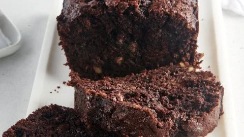 Slice of moist chocolate zucchini bread with chocolate chips on a wooden board