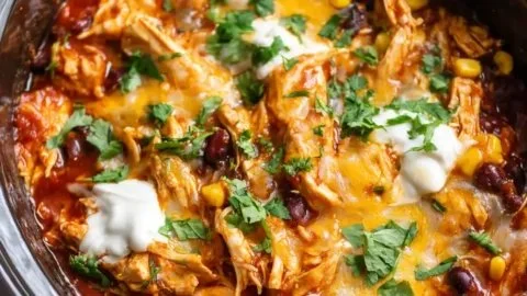 Crockpot chicken enchilada casserole topped with cheese and fresh ingredients