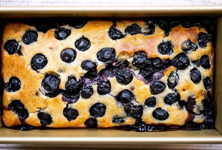 Sliced easy lemon blueberry bread garnished with fresh blueberries and lemon zest.