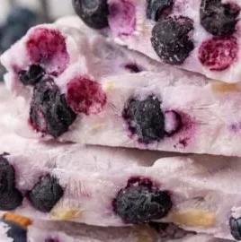 Frozen yogurt bark topped with blueberries and almonds on a wooden surface.