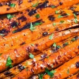Grilled carrots glazed with a sweet sauce on a serving plate.